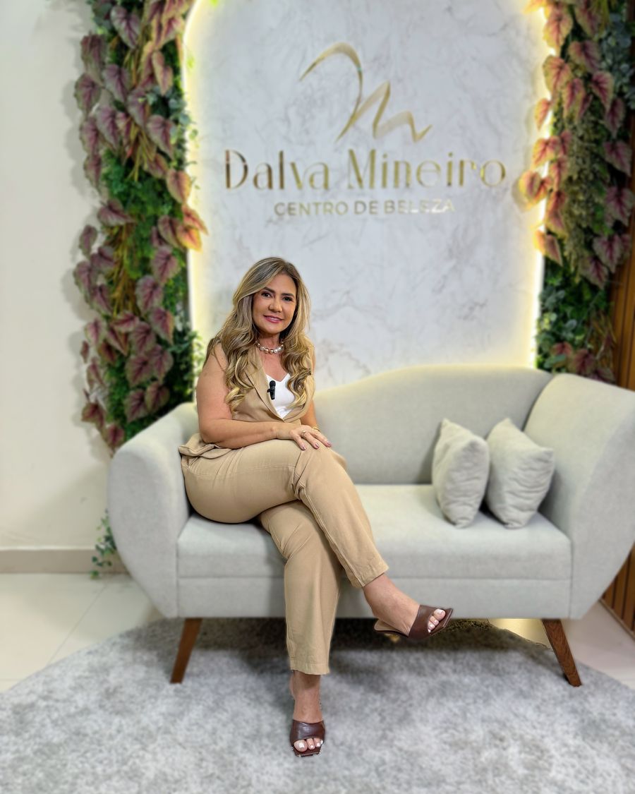 Dalva Mineiro, dona do salão, sentada em frente ao painel em arco com o logo do Centro de Beleza